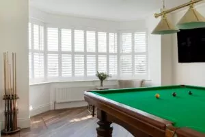plantation shutters in large bay window with pool table Plantation Shutters Project - Your #1 Choice for Shutters NI