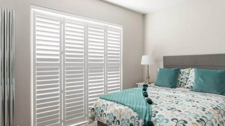 Bedroom with bed and full-height white plantation shutters fitted across the window