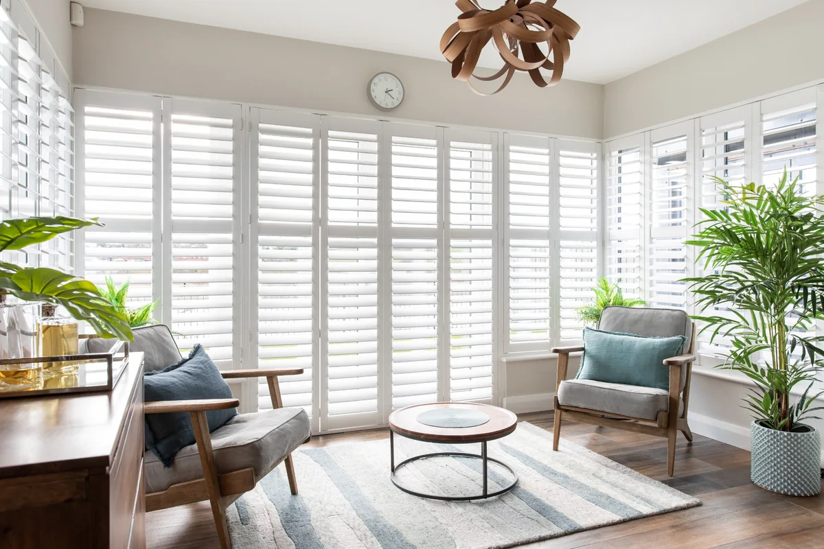 Wide living room with white full height shutters across a large bank of windows