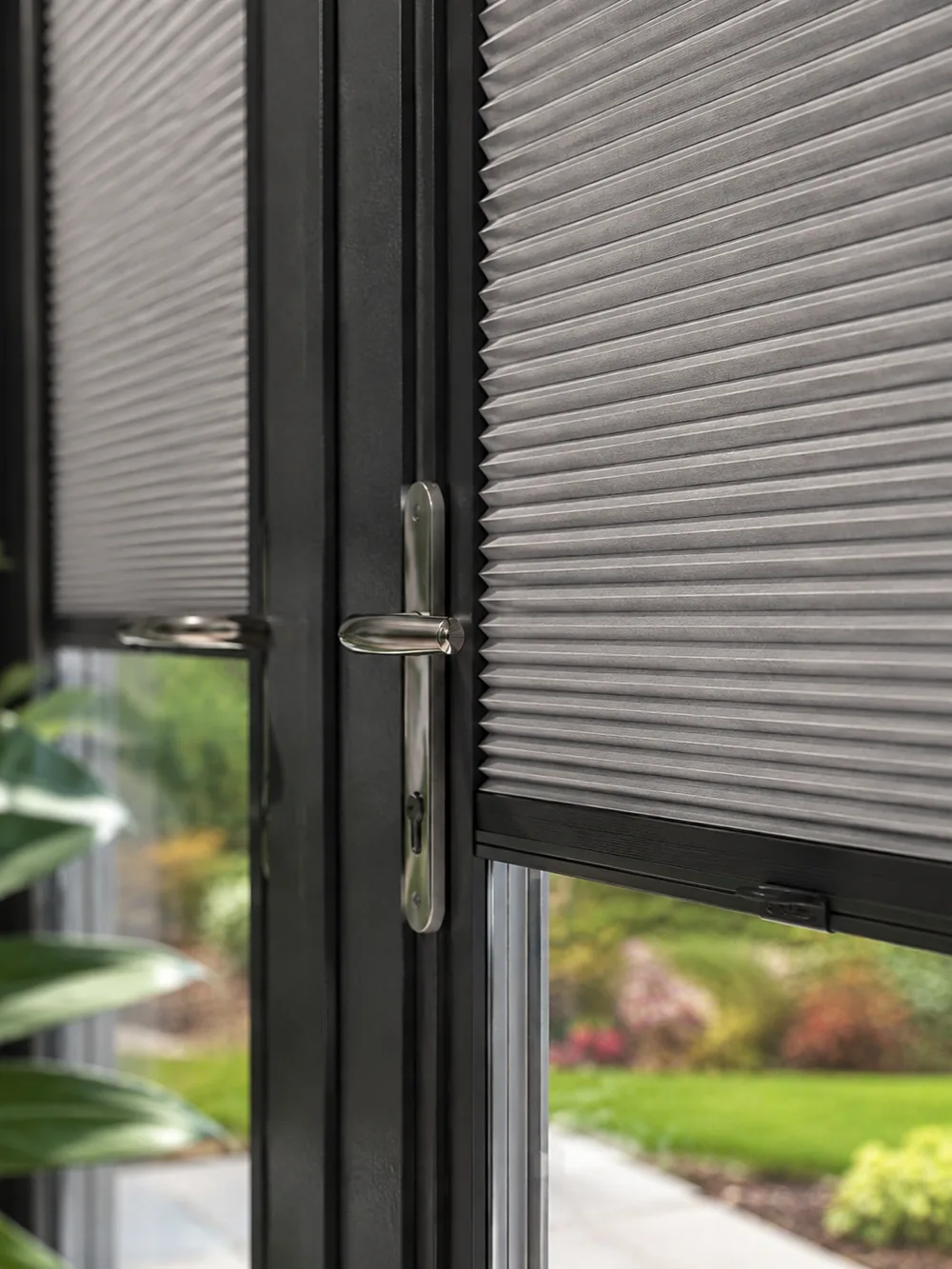 Close-up of a grey cellular Perfect Fit blind held within a dark door frame beside a polished door handle