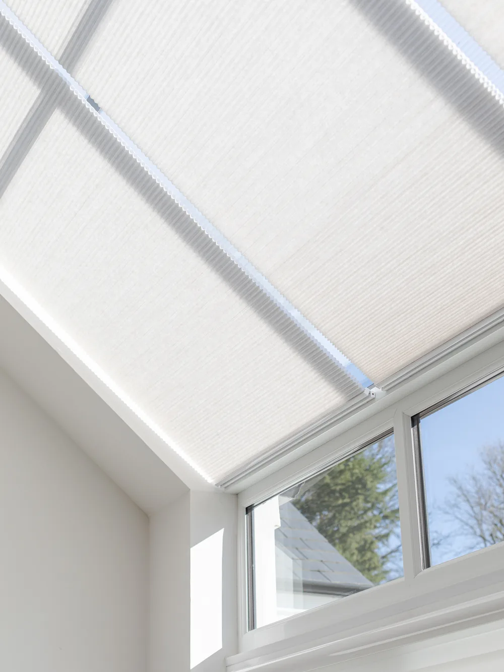 Close-up of a real white cellular roof blind fitted tightly across sloping glazing beside a vertical window