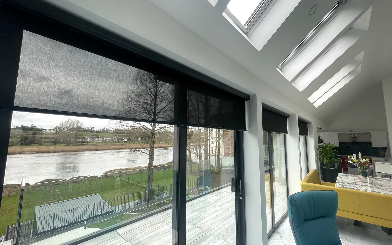 Large motorised roller blinds fitted to black-framed waterfront glazing