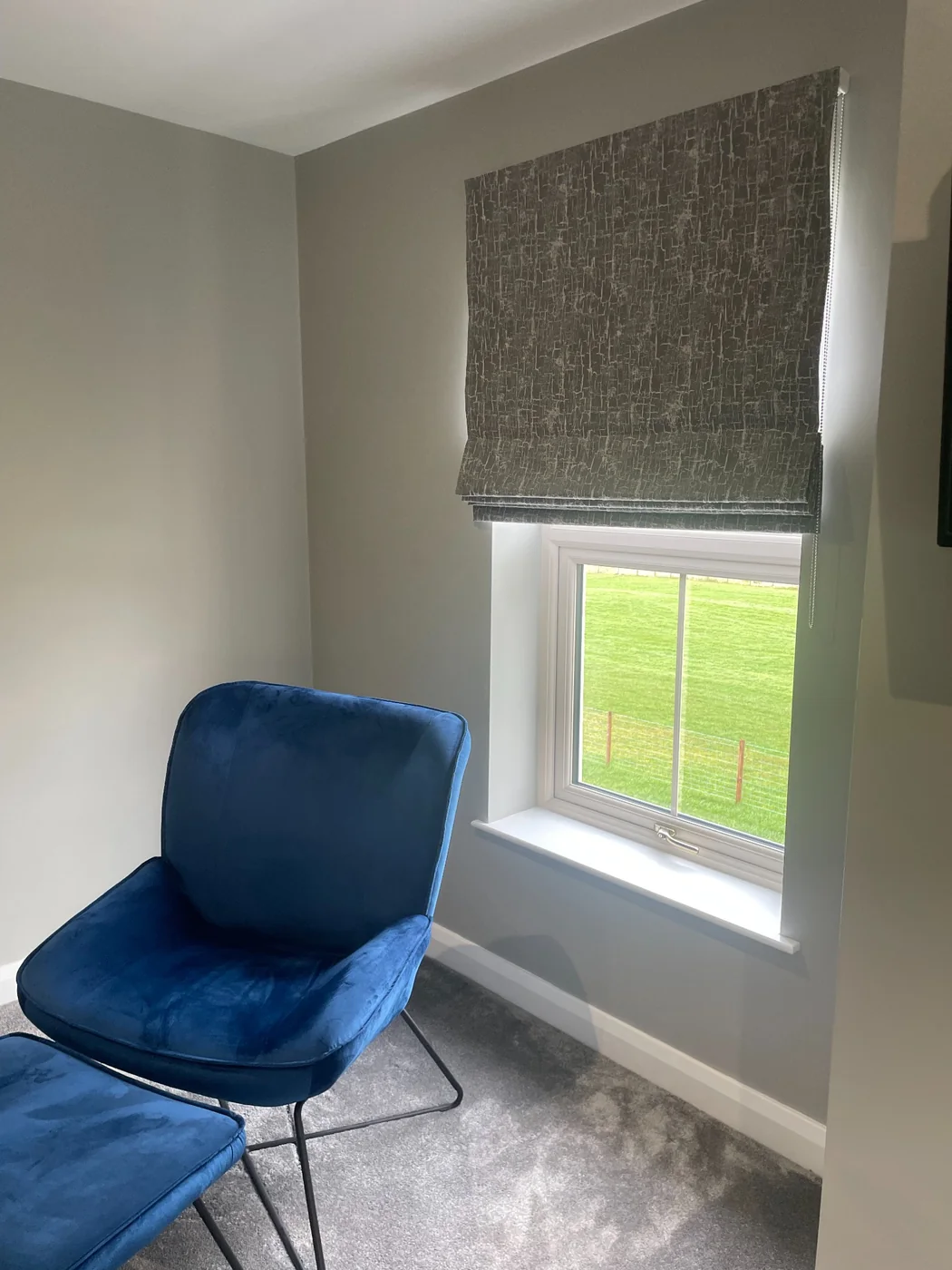 Roman blind in a grey room with a blue chair and countryside view