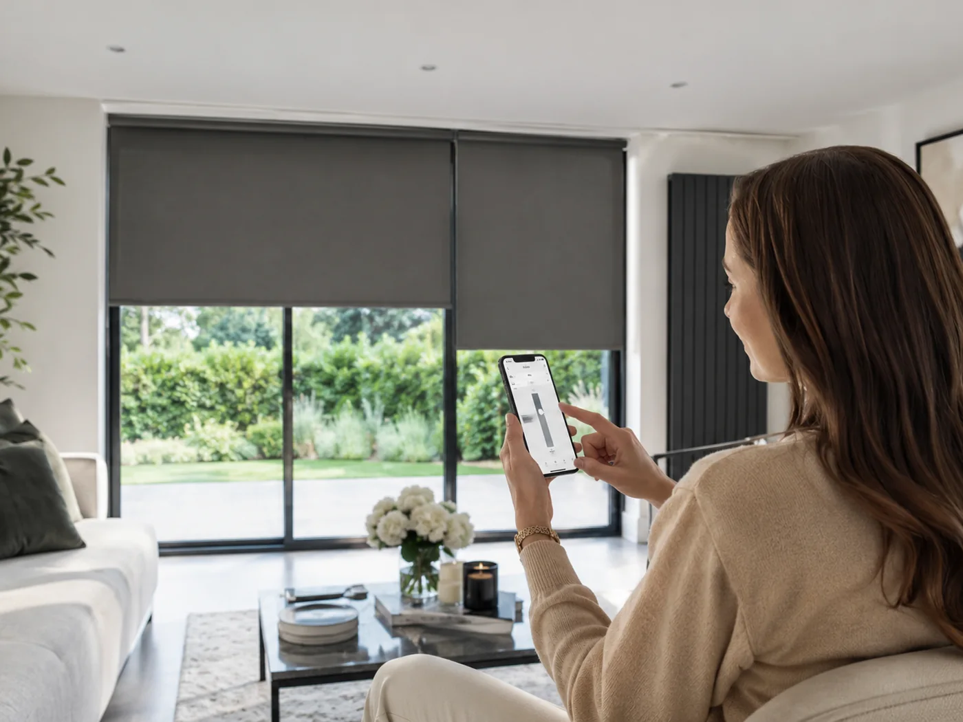 Homeowner using a smartphone to control several motorised blinds in a large living room