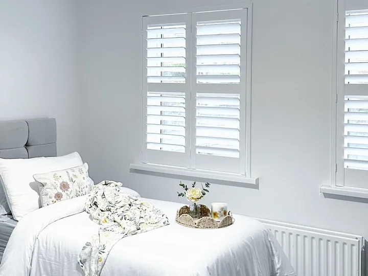 Bright bedroom with white Lumin shutters fitted to two windows