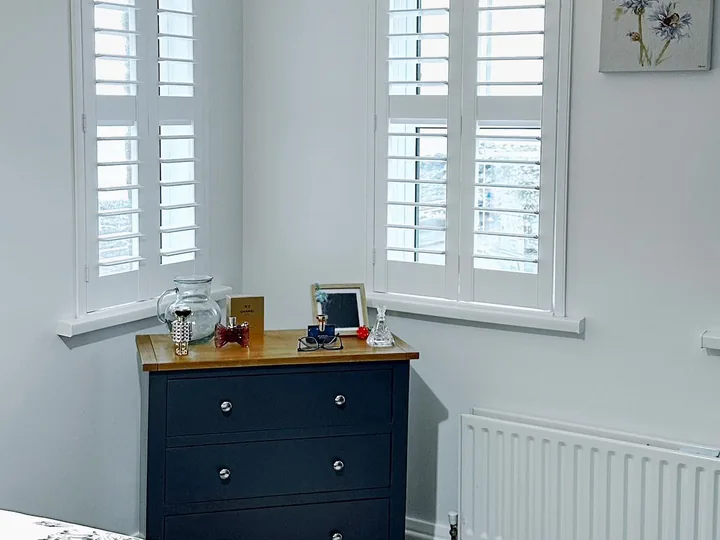 Bedroom corner with two windows fitted with white Lumin shutters
