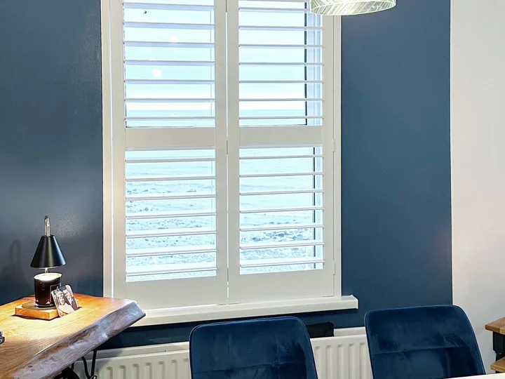 Dining area with white Lumin shutters against a dark blue feature wall