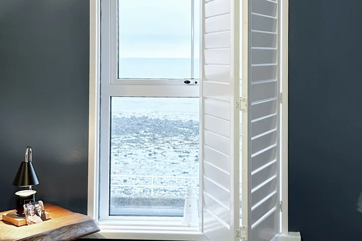 White Lumin shutter panels folded open beside a window with a sea view