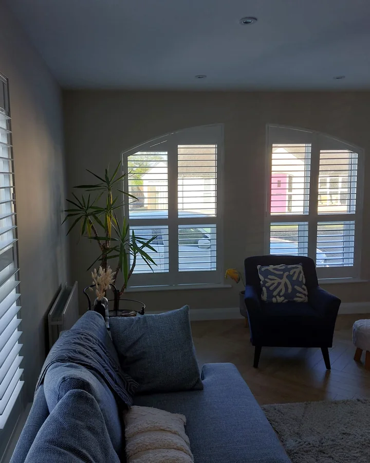 Living room with angled-top windows fitted with white plantation shutters