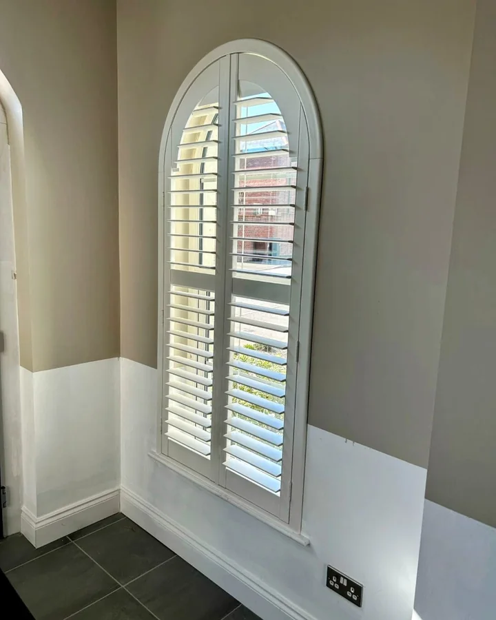Tall arched window fitted with white made-to-measure plantation shutters
