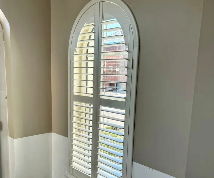 Tall arched window fitted with made-to-measure white plantation shutters in a hallway