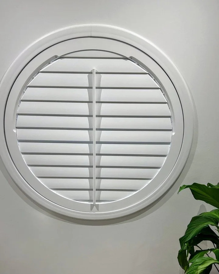 Circular window fitted with made-to-measure white plantation shutters