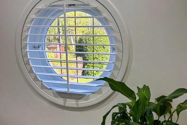 Close view of a circular window fitted with white shaped plantation shutters