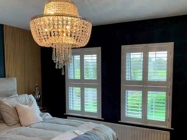 Bedroom with white Tier-on-Tier shutters on two windows against a dark wall