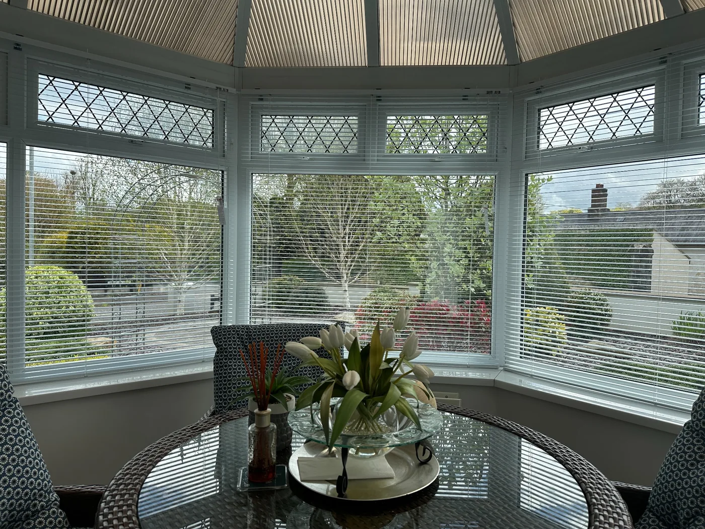 White Venetian blinds fitted around multiple conservatory windows above a glass dining table