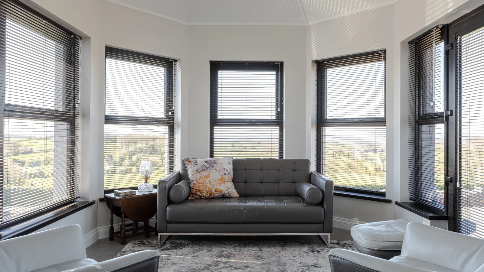 Dark aluminium Venetian blinds fitted around a bright multi-window living room in Northern Ireland