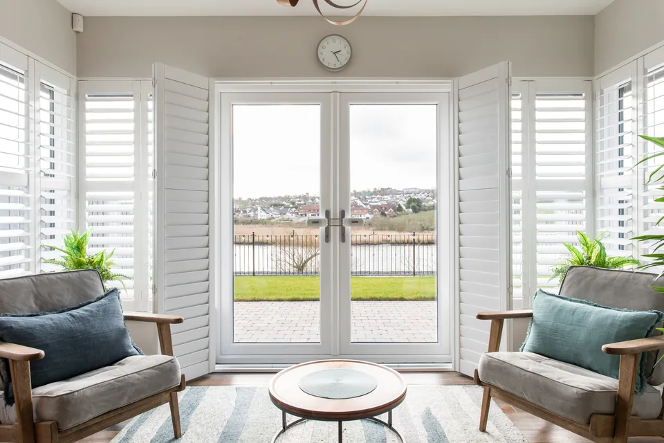 White plantation shutters fitted around glazed doors in a living room